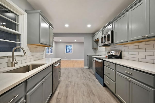 kitchen featuring gray cabinetry, sink, tasteful backsplash, light hardwood / wood-style flooring, and appliances with stainless steel finishes