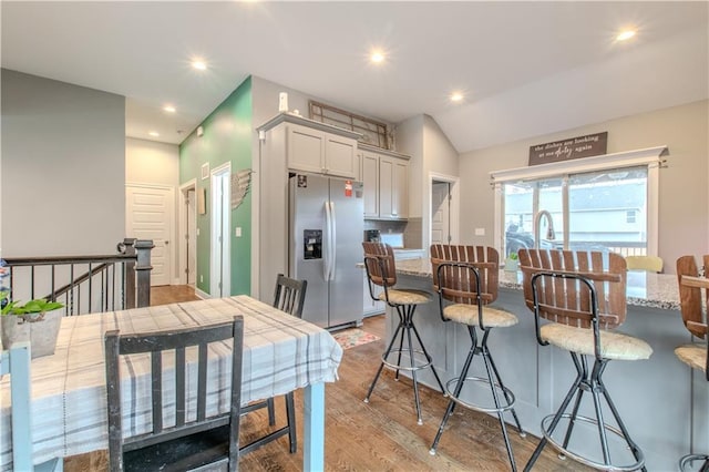 kitchen with white cabinets, light hardwood / wood-style flooring, decorative backsplash, stainless steel fridge, and a breakfast bar area