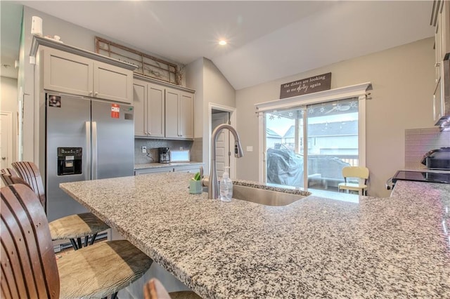 kitchen featuring light stone countertops, sink, a kitchen breakfast bar, backsplash, and stainless steel fridge