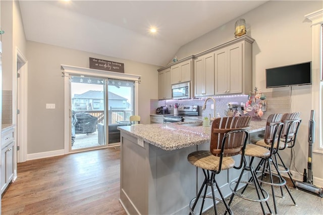 kitchen featuring stainless steel range with electric stovetop, a breakfast bar, lofted ceiling, gray cabinets, and tasteful backsplash