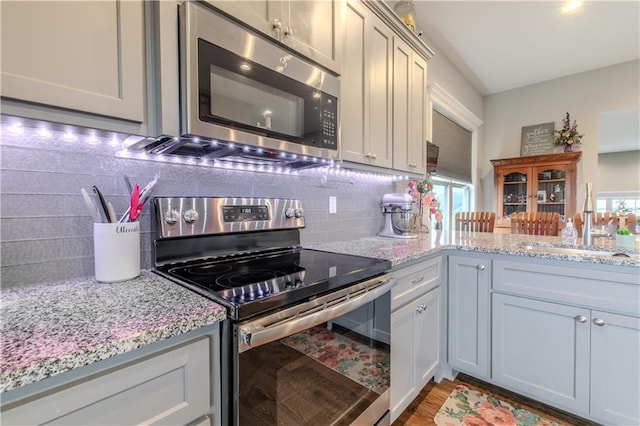 kitchen featuring decorative backsplash, stainless steel appliances, light stone counters, and sink