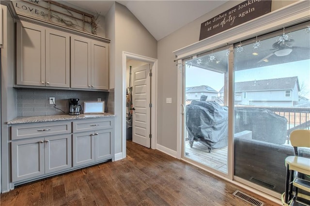 kitchen with a wealth of natural light, light stone counters, backsplash, vaulted ceiling, and gray cabinets