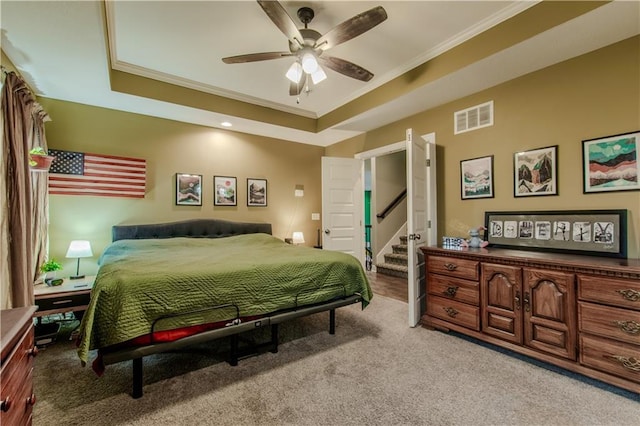 bedroom featuring ceiling fan, light colored carpet, crown molding, and a tray ceiling