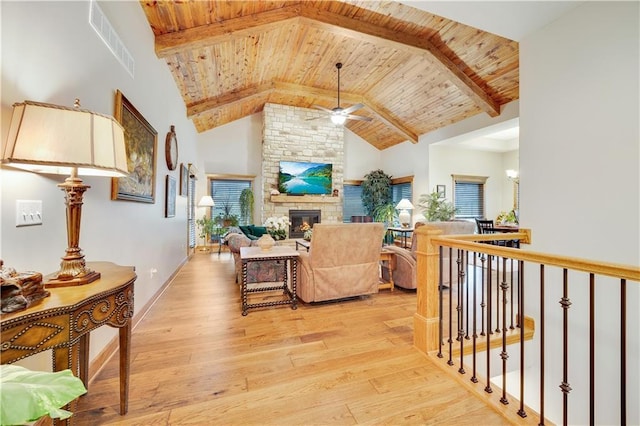 living room featuring wooden ceiling, a stone fireplace, ceiling fan, beam ceiling, and light hardwood / wood-style floors