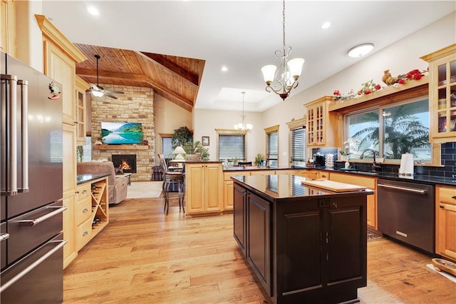 kitchen featuring a center island, hanging light fixtures, stainless steel appliances, a stone fireplace, and ceiling fan with notable chandelier