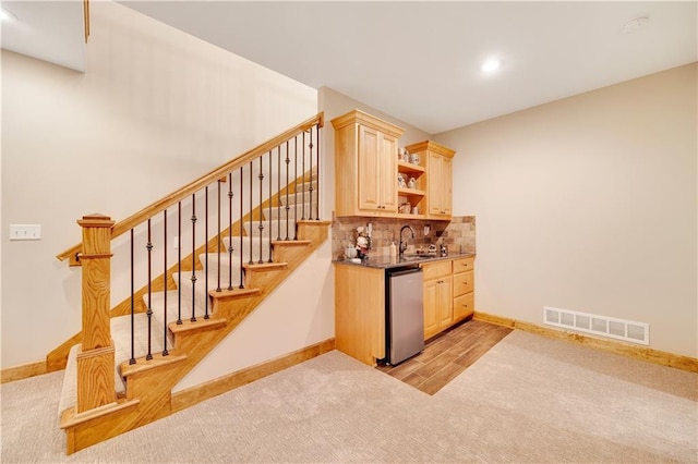 bar with backsplash, sink, stainless steel dishwasher, light brown cabinetry, and light hardwood / wood-style floors