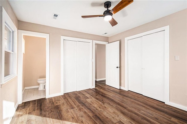 unfurnished bedroom with wood finished floors, visible vents, baseboards, ensuite bath, and multiple closets