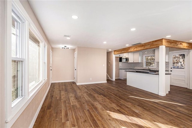 kitchen with stainless steel microwave, tasteful backsplash, dark countertops, dark wood-style floors, and baseboards