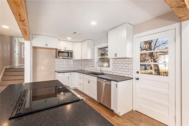 kitchen featuring a sink, backsplash, dark countertops, wood finished floors, and appliances with stainless steel finishes