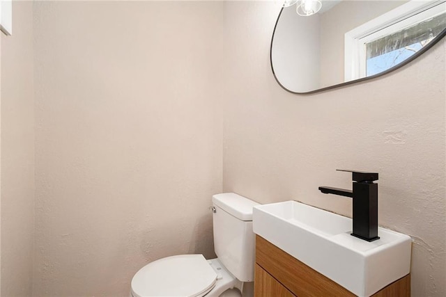 bathroom featuring toilet, vanity, and a textured wall