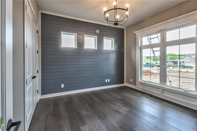 unfurnished room with wooden walls, dark hardwood / wood-style flooring, a wealth of natural light, and an inviting chandelier