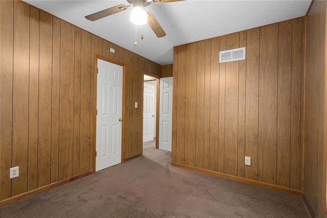 unfurnished bedroom with carpet, ceiling fan, and wood walls