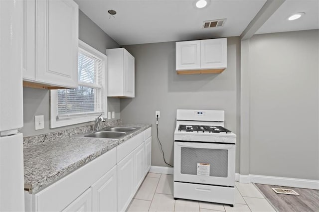 kitchen with white cabinets, white gas stove, light tile patterned floors, and sink