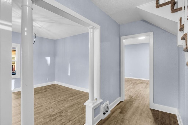 hall featuring lofted ceiling, wood-type flooring, and ornate columns