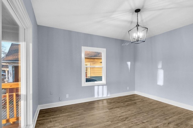 spare room featuring dark wood-type flooring, a healthy amount of sunlight, and an inviting chandelier