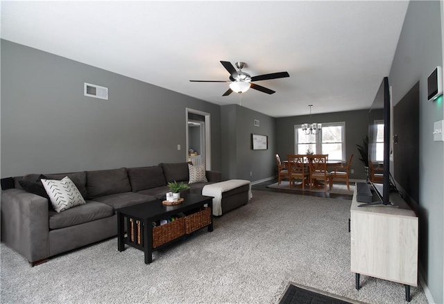 living room featuring light colored carpet, visible vents, baseboards, and ceiling fan with notable chandelier