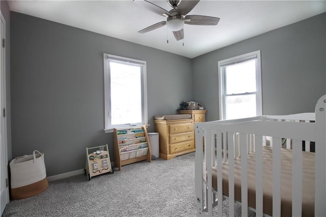 bedroom featuring a ceiling fan, a nursery area, carpet flooring, and baseboards