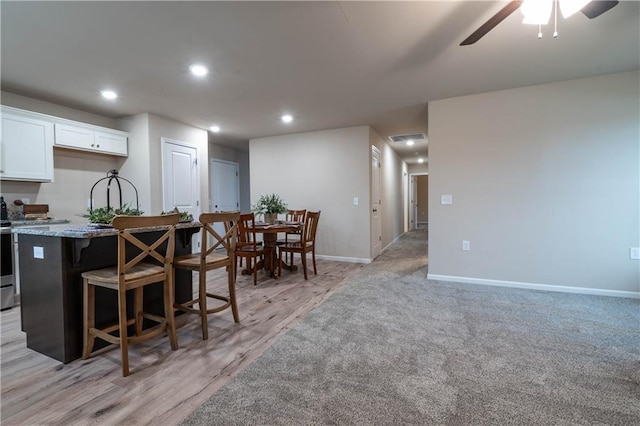 kitchen with light stone countertops, a center island, ceiling fan, a kitchen breakfast bar, and white cabinets