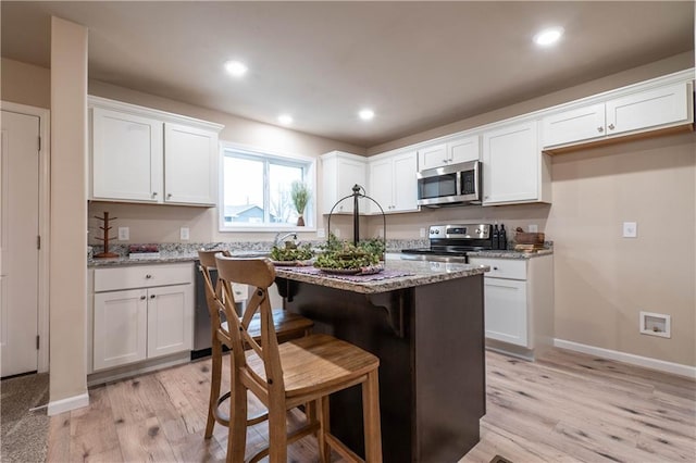 kitchen with light hardwood / wood-style floors, light stone countertops, white cabinetry, and stainless steel appliances