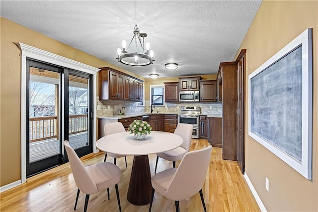 dining space with a textured ceiling, light wood-type flooring, a notable chandelier, and sink