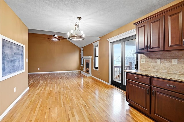 kitchen featuring light stone countertops, tasteful backsplash, pendant lighting, ceiling fan with notable chandelier, and light wood-type flooring