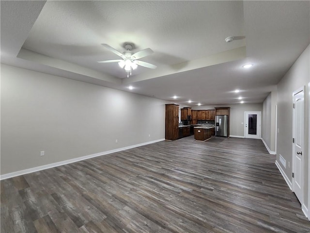 unfurnished living room with dark wood-style floors, a raised ceiling, baseboards, and a ceiling fan