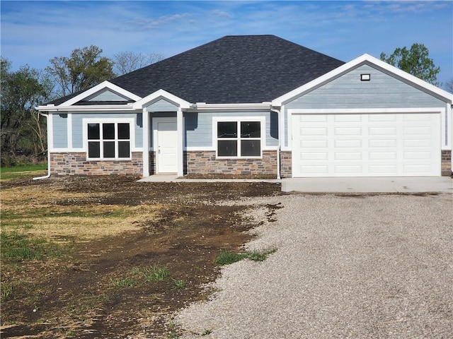 view of front of home with gravel driveway, stone siding, a shingled roof, and a garage