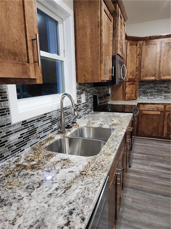 kitchen featuring light stone counters, tasteful backsplash, a sink, stainless steel appliances, and dark wood-style floors
