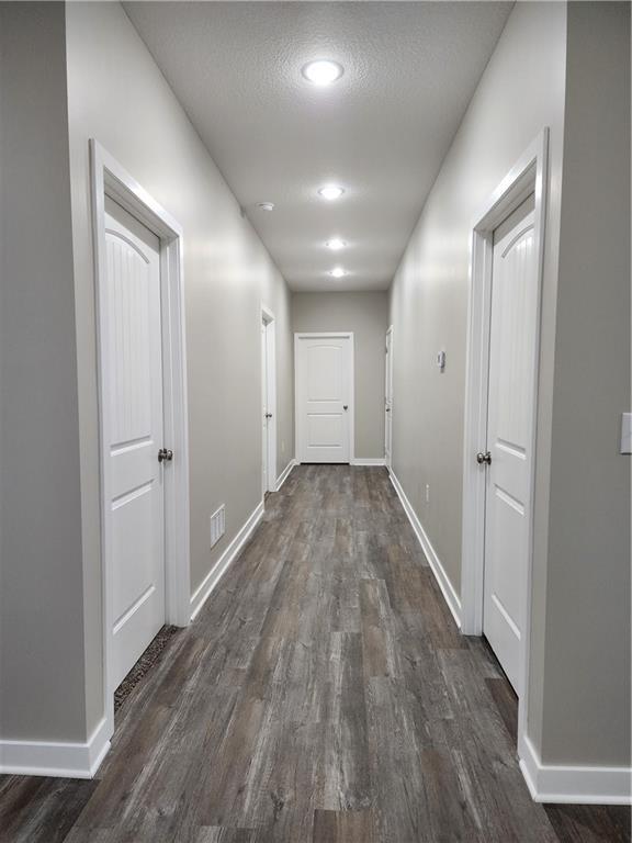 hall with a textured ceiling, dark wood finished floors, visible vents, and baseboards