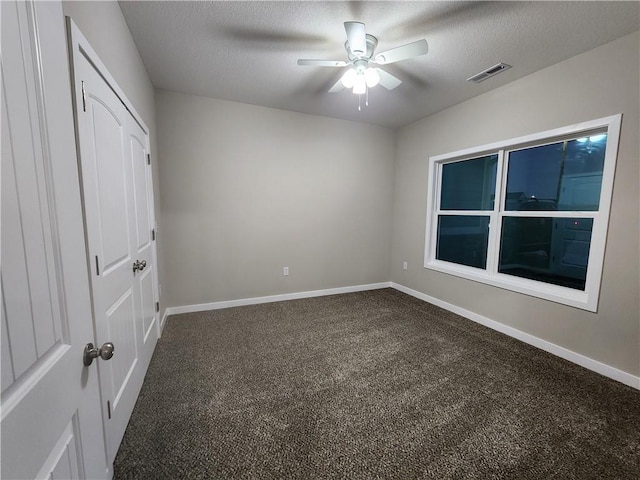 unfurnished bedroom with a textured ceiling, dark colored carpet, visible vents, and baseboards