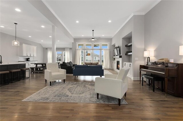 living room with ceiling fan, dark wood finished floors, a lit fireplace, ornamental molding, and recessed lighting