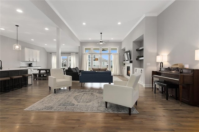living area featuring recessed lighting, dark wood-style flooring, a warm lit fireplace, ceiling fan, and crown molding