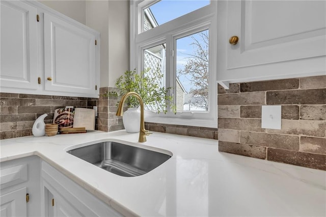 kitchen featuring decorative backsplash, white cabinetry, light stone countertops, and sink