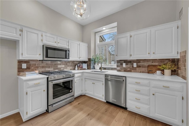 kitchen with sink, hanging light fixtures, stainless steel appliances, decorative backsplash, and white cabinets