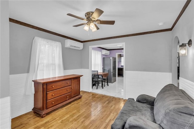 living area with a wall mounted air conditioner, ceiling fan, light wood-type flooring, and ornamental molding