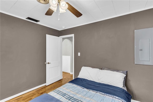 bedroom with hardwood / wood-style floors, ceiling fan, ornamental molding, and electric panel