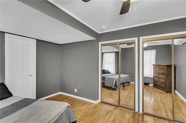 bedroom with hardwood / wood-style flooring, ceiling fan, and two closets