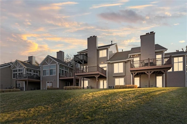 back house at dusk featuring a deck and a lawn