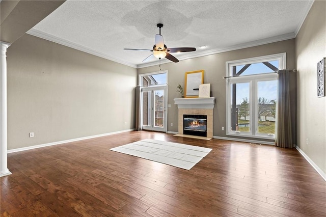 unfurnished living room featuring crown molding, dark hardwood / wood-style floors, a tiled fireplace, and ornate columns