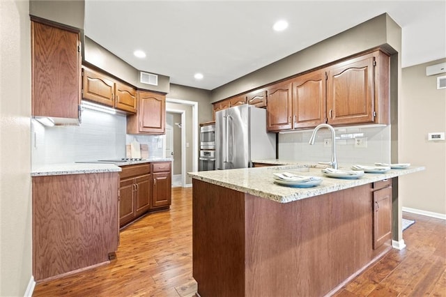 kitchen with sink, light stone counters, light hardwood / wood-style flooring, kitchen peninsula, and stainless steel appliances