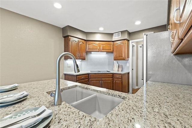 kitchen with sink, stainless steel fridge, black electric stovetop, light stone countertops, and backsplash