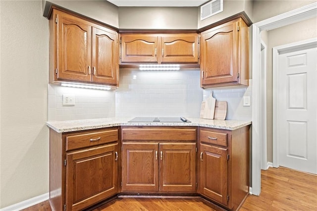 kitchen with light stone countertops, backsplash, black electric cooktop, and light hardwood / wood-style floors