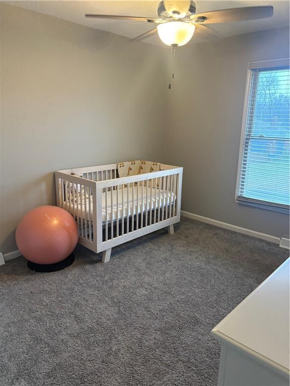 bedroom with ceiling fan, a nursery area, and dark carpet