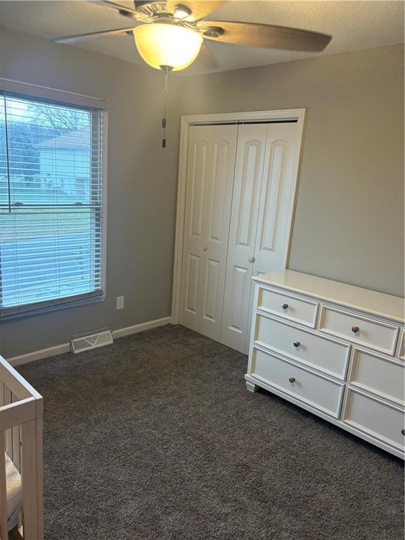 unfurnished bedroom featuring dark colored carpet, ceiling fan, multiple windows, and a closet