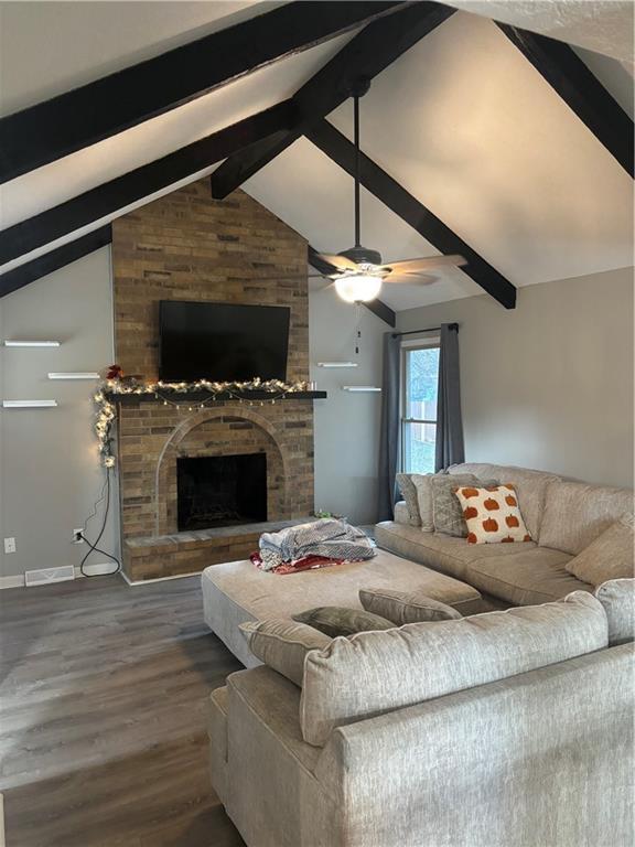 living room with dark hardwood / wood-style flooring, lofted ceiling with beams, a brick fireplace, and ceiling fan