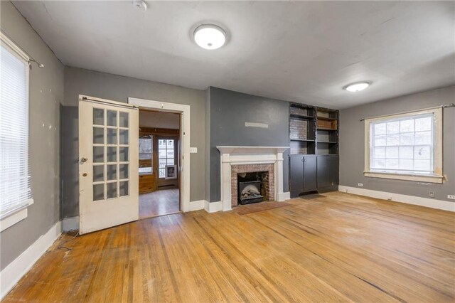 unfurnished living room featuring french doors, wood-type flooring, and a brick fireplace