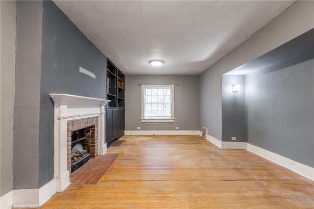 unfurnished living room with built in shelves, a fireplace, and light hardwood / wood-style flooring