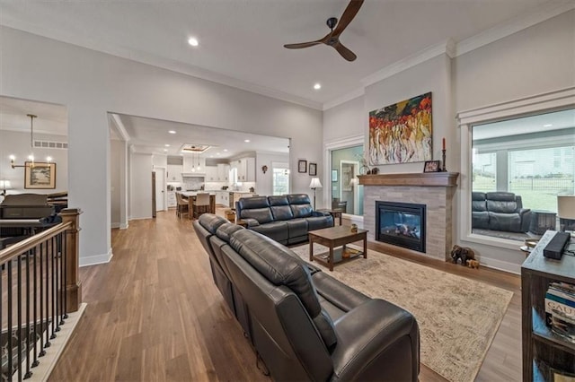 living room featuring ornamental molding, a fireplace, ceiling fan with notable chandelier, and light wood-type flooring