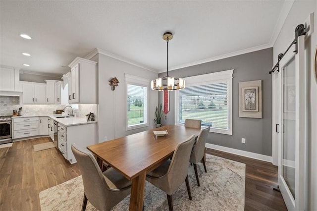 dining room with sink, hardwood / wood-style flooring, crown molding, a barn door, and an inviting chandelier