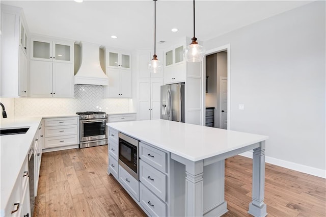 kitchen featuring pendant lighting, premium range hood, stainless steel appliances, a center island, and white cabinets